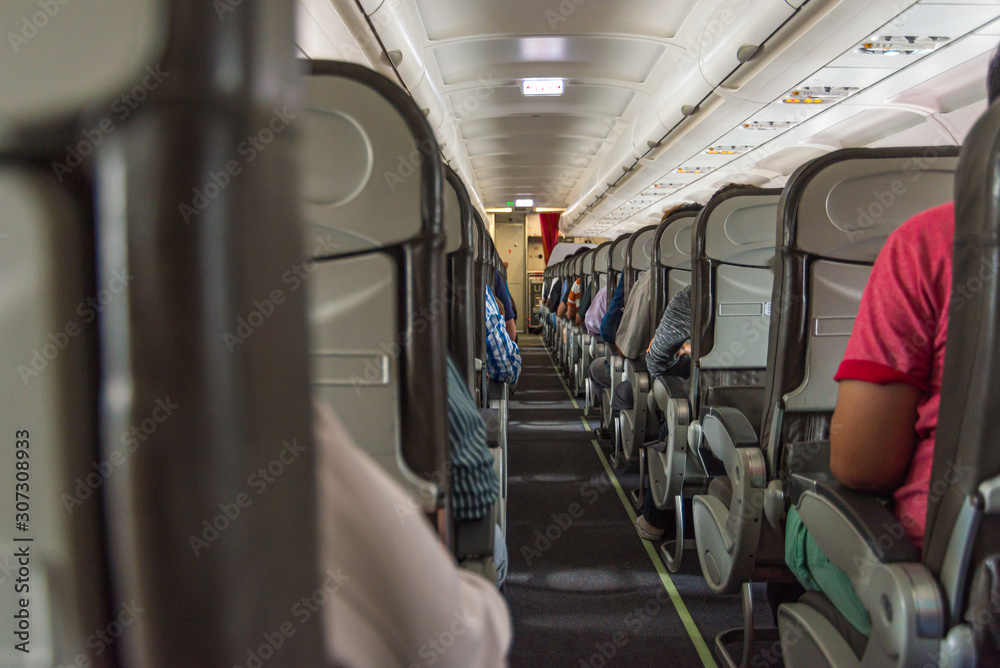 Obraz premium Walking aisle and passengers in economy class cabin on airplane