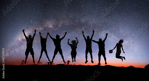 Silhouette of friends jumping on the sand dune against milky way galaxy