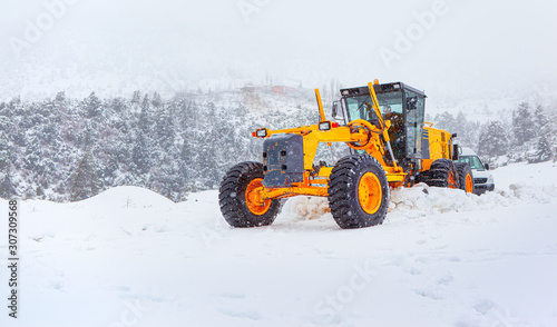 Bulldozer cleans snow-covered road through the forest.