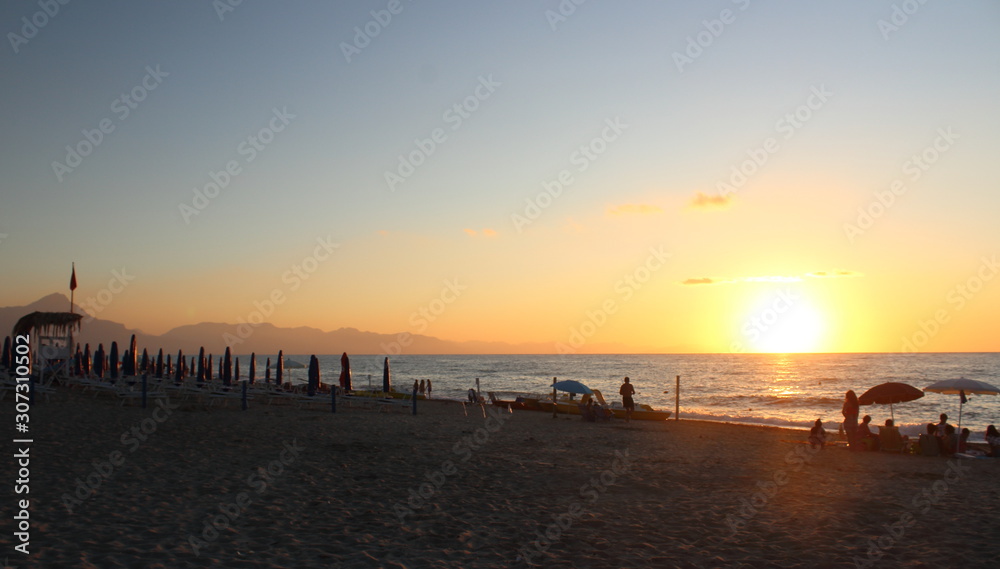 the sun setting behind the promontory with the sea in the foreground the sun setting behind the promontory with the sea in the foreground