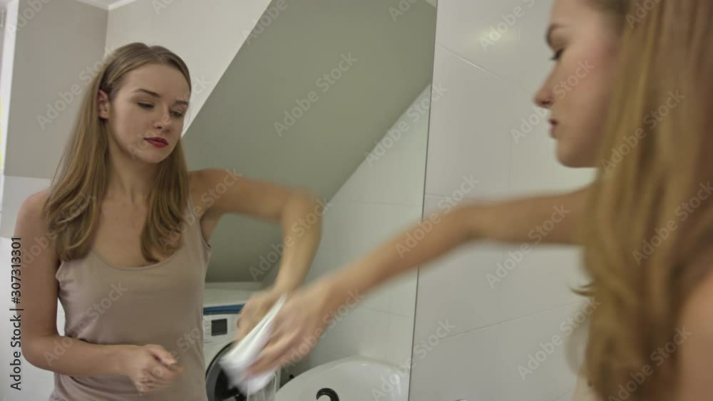 Young woman cleans the bathroom mirror at her home. Doing domestic cleaning with cloth. Household concept. Young woman cleans the bathroom mirror at her home. Doing domestic cleaning with cloth. Household concept.