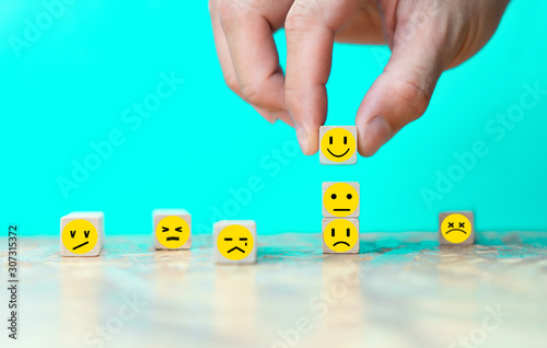 Businessman chooses a happy emoticon icons face on wooden block.