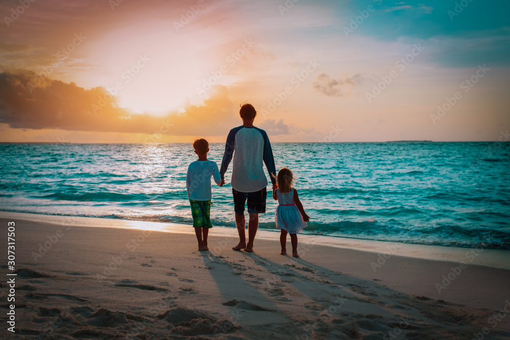 father and kids walking on beach at sunset
