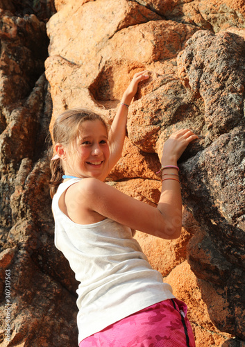 smiling little girl as she climbs the red rock of the mountain
