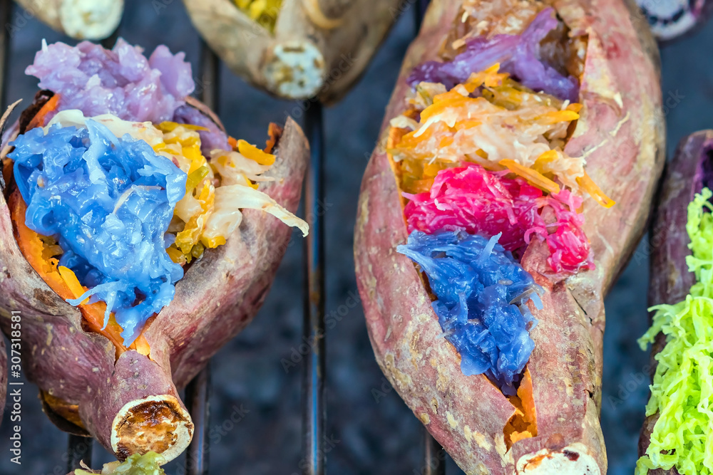 Colorful of many Thai traditional desserts stuffed in grilled yams on stove for sale on street food.