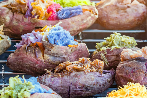 Colorful of many Thai traditional desserts stuffed in grilled yams on stove for sale on street food. photo