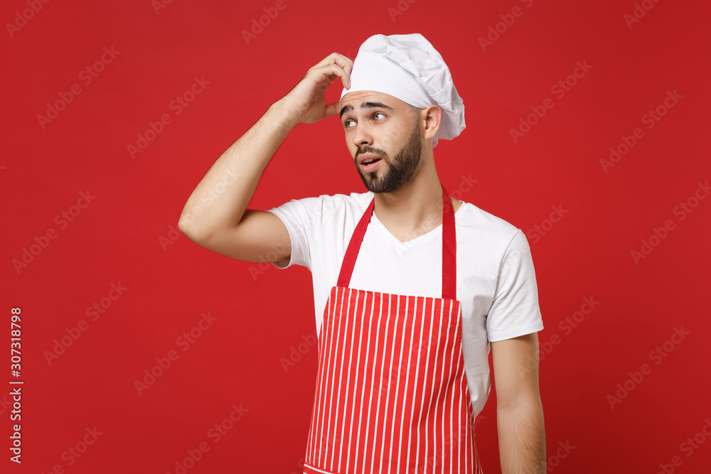 Pensive young male chef cook baker man in striped apron white t-shirt toque  chefs hat