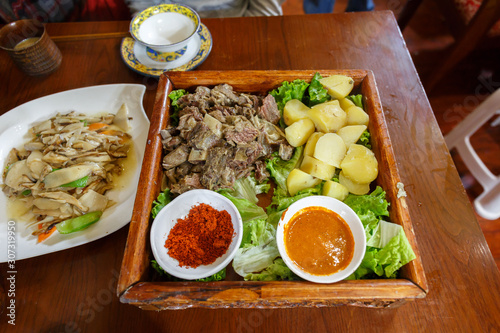 LHASA, TIBET / CHINA - July 29, 2017: Traditional tibetan food on a wooden plate - served in a restaurant near Barkhor Street / Jokhang temple. On the plate: yak meat, potatos, salad, sauce and spice.