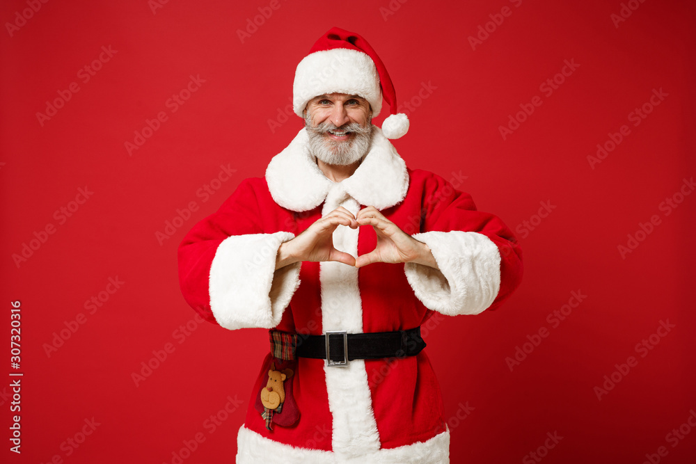 Elderly gray-haired mustache bearded Santa man in Christmas hat posing isolated on red background. Happy New Year 2020 celebration holiday concept. Mock up copy space. Showing shape heart with hands. Elderly gray-haired mustache bearded Santa man in Christmas hat posing isolated on red background. Happy New Year 2020 celebration holiday concept. Mock up copy space. Showing shape heart with hands.