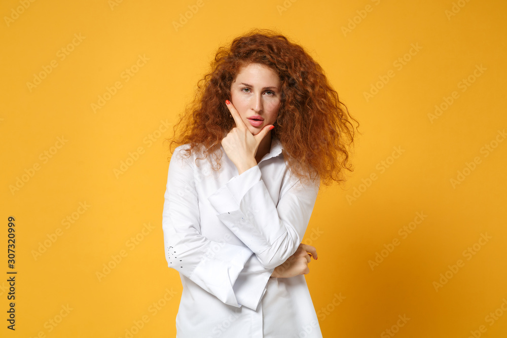 Confident young redhead woman girl in white shirt posing isolated on yellow orange background, studio portrait. People sincere emotions lifestyle concept. Mock up copy space. Put hand prop up on chin.