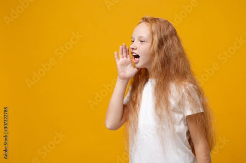 Side view of little ginger kid girl 12-13 years old in white t-shirt isolated on yellow background children studio portrait. Childhood lifestyle concept. Mock up copy space. Scream with hand gesture.