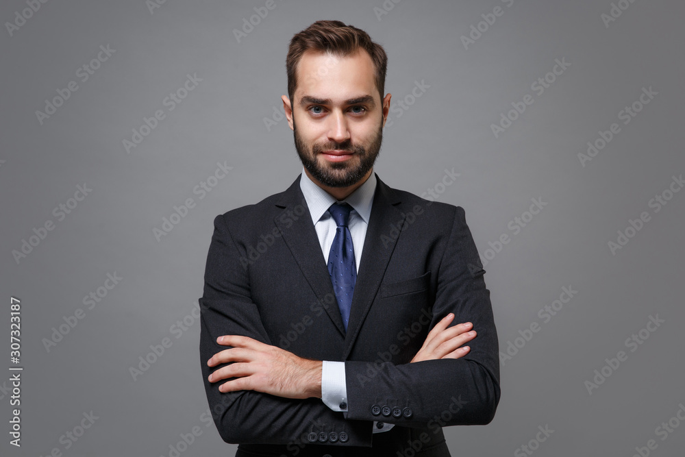 Attractive young business man in classic black suit shirt tie posing isolated on grey background studio portrait. Achievement career wealth business concept. Mock up copy space. Holding hands crossed. - obrazy, fototapety, plakaty 