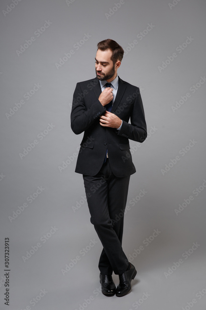 Attractive young business man in classic black suit shirt tie posing isolated on grey background studio portrait. Achievement career wealth business concept. Mock up copy space. Straightening tie. Attractive young business man in classic black suit shirt tie posing isolated on grey background studio portrait. Achievement career wealth business concept. Mock up copy space. Straightening tie.