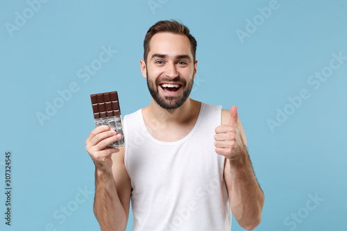 Bearded young man 20s years old in white shirt hold in hand chocolate bar isolated on blue pastel wall background, studio portrait. Skin care healthcare cosmetic procedures concept. Mock up copy space