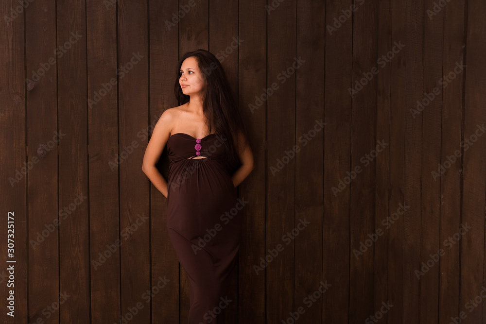 Pregnant woman in brown dress holds hands on belly on a dark brown background. Pregnancy, maternity, expectation concept. Beautiful tender mood photo of pregnancy Pregnant woman in brown dress holds hands on belly on a dark brown background. Pregnancy, maternity, expectation concept. Beautiful tender mood photo of pregnancy