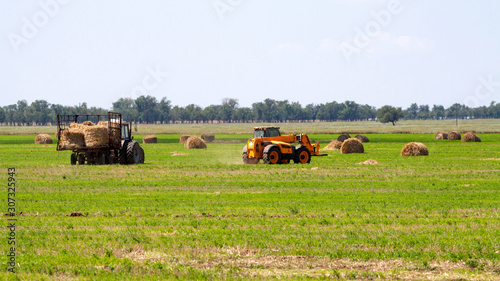 Tractor loading hay bales on truck agricultural works