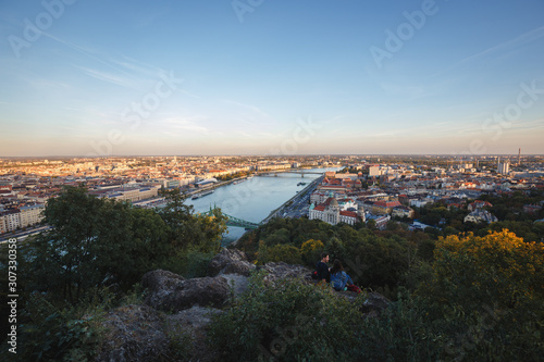 A couple sits on the rock side of the mountain to enjoy the dusk scenery of Budapest