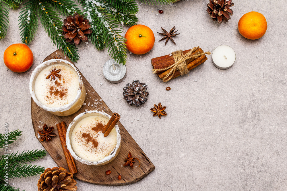 Eggnog with cinnamon and nutmeg for Christmas and winter holidays. Homemade beverage in glasses with spicy rim. Tangerines, candles, gift. Stone concrete background Eggnog with cinnamon and nutmeg for Christmas and winter holidays. Homemade beverage in glasses with spicy rim. Tangerines, candles, gift. Stone concrete background