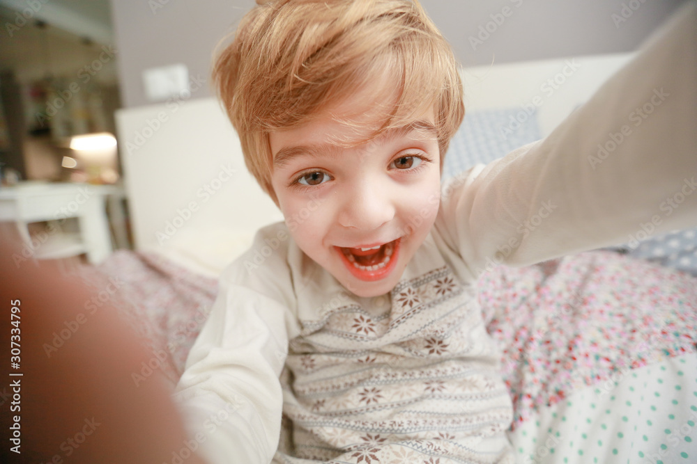 The boy in pajamas preschool age sits on bed and photographing himself themselves. The boy in pajamas preschool age sits on bed and photographing himself themselves.