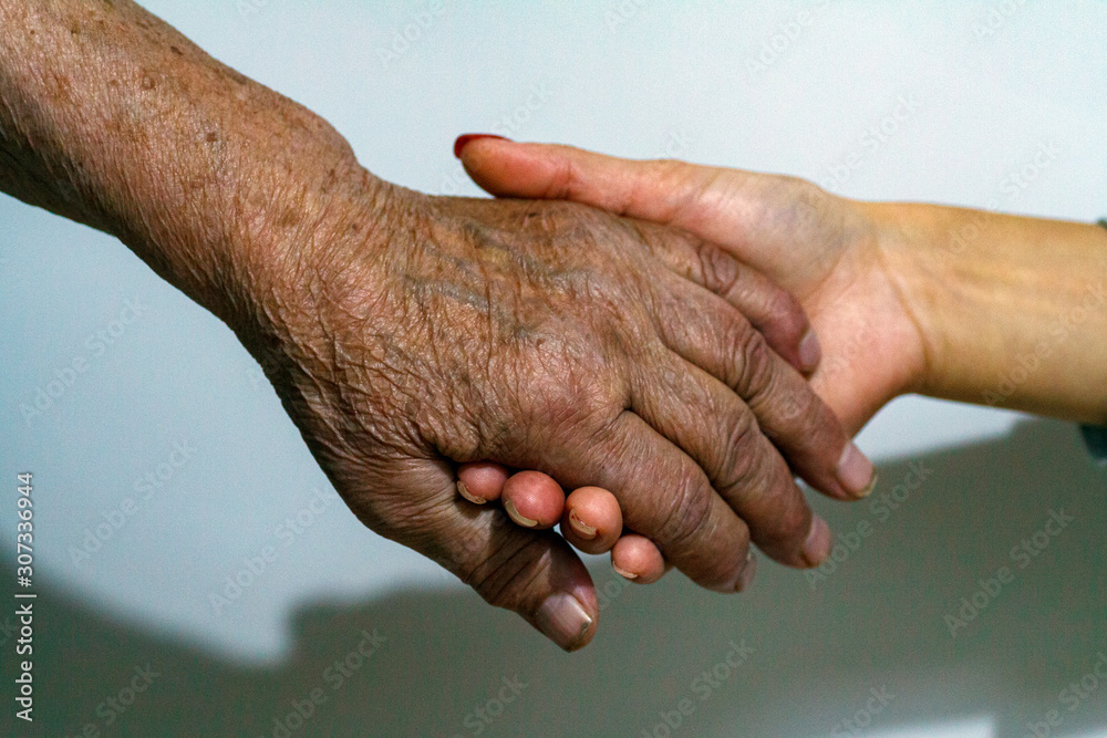Fototapeta premium An elderly woman grandmother and a young girl hold hands. Support for the elderly from young people and children. Caring for retired old people.