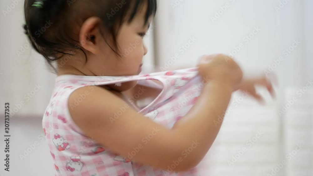Little Asian baby girl, 2 years old, being proud and happy as she eventually can successfully put on a shirt by herself