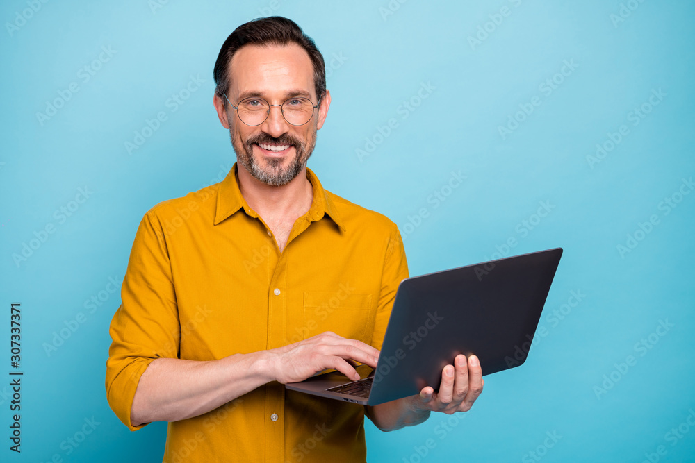 Portrait of positive cool mature man hold his computer work text type chatting with family colleagues wear good looking clothes isolated over blue color background Portrait of positive cool mature man hold his computer work text type chatting with family colleagues wear good looking clothes isolated over blue color background