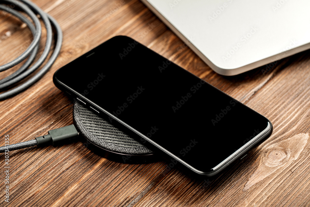 Wireless charging lies next to the computer on a stylish wooden table Wireless charging lies next to the computer on a stylish wooden table