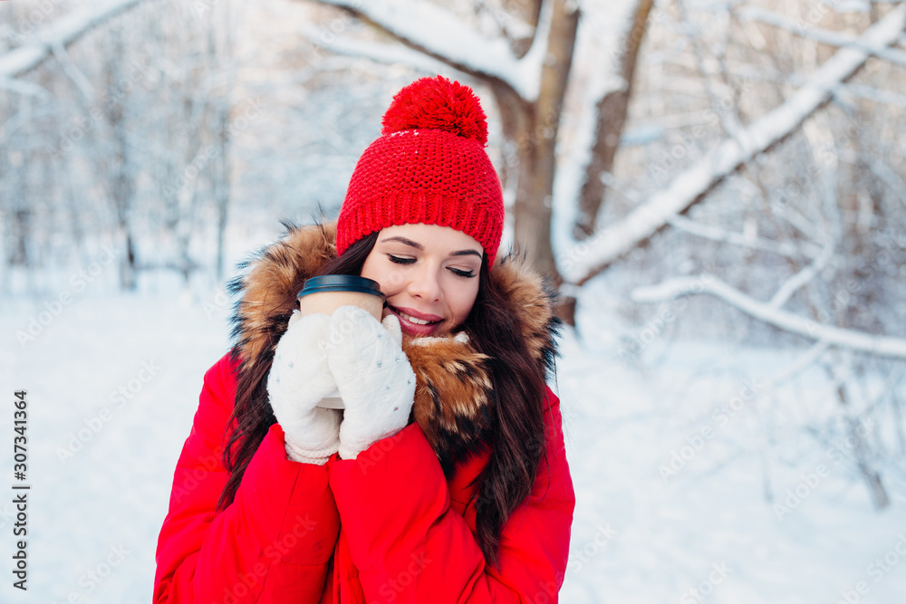 Cheerful brunette in winter fashion holding disposable cup of coffee in winter park