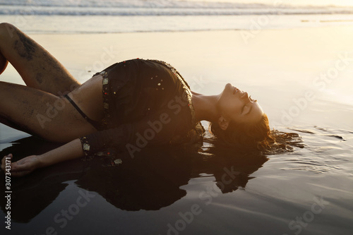 Sexy woman wearing black tunic is posing on the beach with black sand