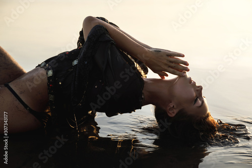 Sexy woman wearing black tunic is posing on the beach with black sand