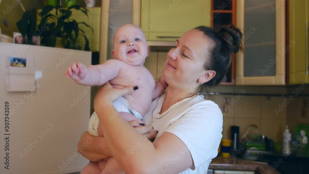 Young mother holding her son smiling to him and making funny grimace in the kitchen. Young mother holding her son smiling to him and making funny grimace in the kitchen.