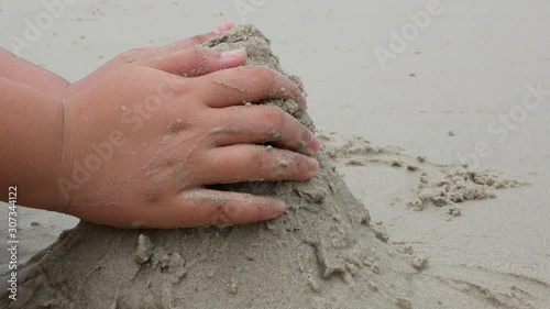 Kid's hands piling up wet sand, building a hill at a beachside - children's sand playing helps develop their eye-hand coordination and imagination
