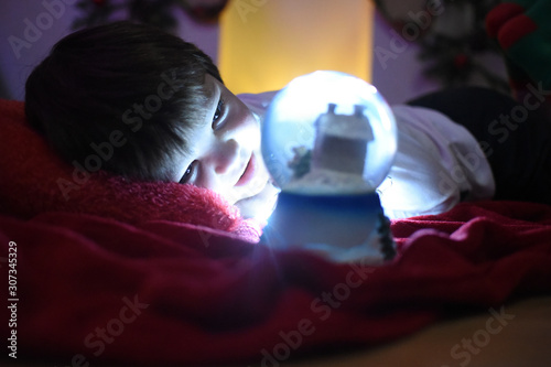 Boy looking a glass snow ball under a Christmas tree. Child with a snow ball with a New Year