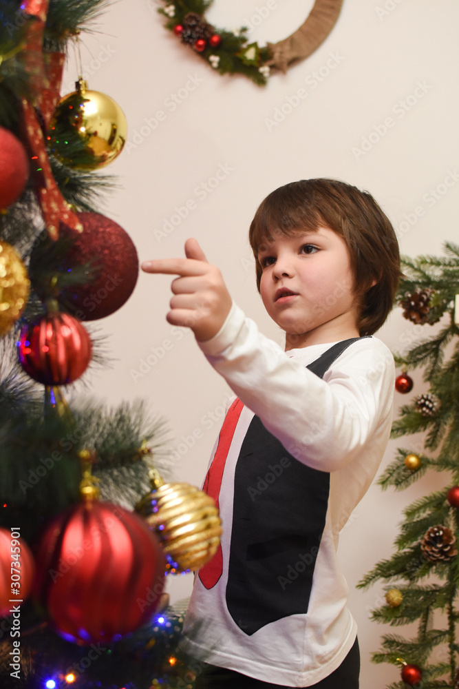 Portrait of happy boy decorating Christmas tree. Cheerful child under a fir tree play for Christmas
