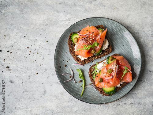 Healthy toasts with rye bread with cream cheese, salmon, fresh cucumber, capers, sesame seeds, black pepper and arugula on plate. Top view photo