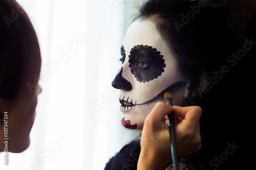 Halloween. Make-up artist making woman up as skeleton for Mexican Day of Dead