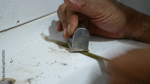 A handy man's hands holding a metal saw and cutting off an old rusty stripped-screw toilet seat joint, as he tried to replace them
