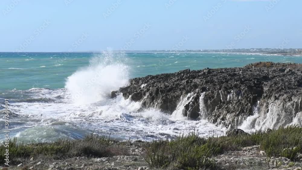Panoramic view on waves dashing on a shore of black rocks in a touristic resort in Puglia, Italy. Clear water on a sunny and windy day crushing on the stony shore Panoramic view on waves dashing on a shore of black rocks in a touristic resort in Puglia, Italy. Clear water on a sunny and windy day crushing on the stony shore