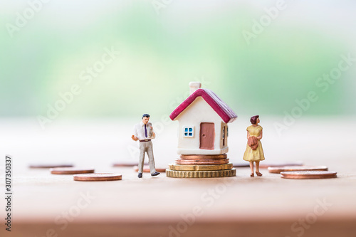 selective focus of miniature angry woman with miniature man and mini house on stack coins over blurred green garden background  for Asset management after divorce concept.
