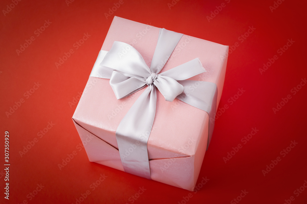 Single pink gift box with silver ribbon on red background.