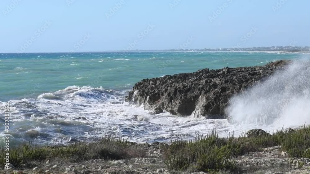 Panoramic view on waves dashing on a shore of black rocks in a touristic resort in Puglia, Italy. Clear water on a sunny and windy day crushing on the stony shore Panoramic view on waves dashing on a shore of black rocks in a touristic resort in Puglia, Italy. Clear water on a sunny and windy day crushing on the stony shore