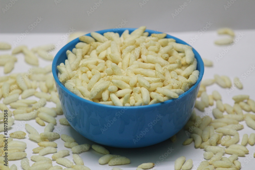 Puffed rice on the blue bowl with white background and some buffed rice are spreading on the floor Puffed rice on the blue bowl with white background and some buffed rice are spreading on the floor