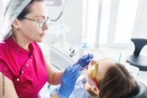 In the dentist's office. A female dentist in glasses is preparing to make a cast of the jaw of a young girl patient. Care clean mouth