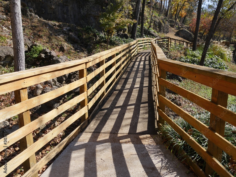 Shadows falling on a  wooden walkway with railings by the side of a flowing spring in autumn