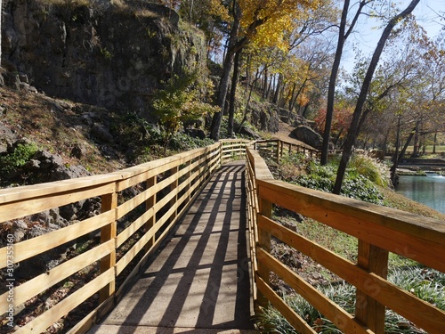 Wooden walkway with railings by the side of a flowing spring in autumn