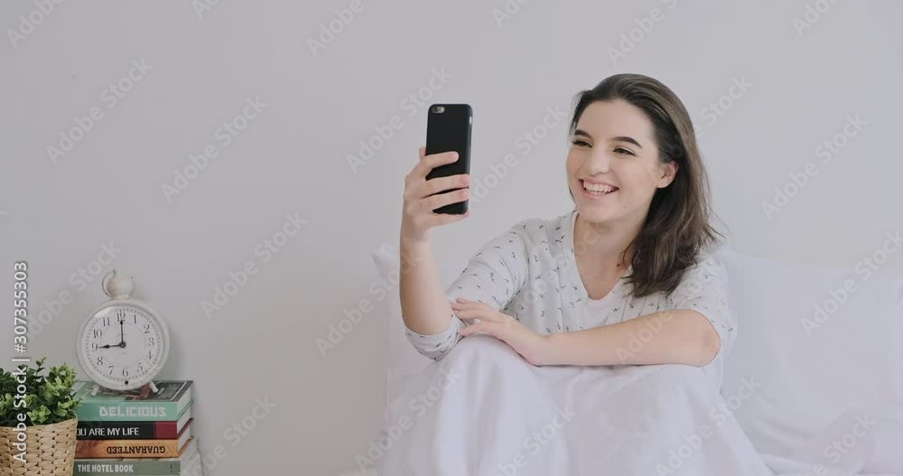 Happy woman in bed using mobile phone. Caucasian girl, having video call and kiss. Wide shot with copy space. Happy woman in bed using mobile phone. Caucasian girl, having video call and kiss. Wide shot with copy space.
