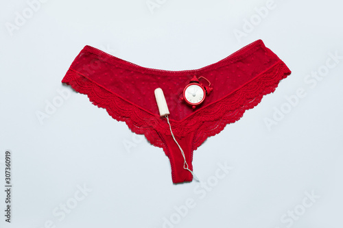Womens lace red panties with medical female tampon against critical days on a blue background. Menstruation, means of protection