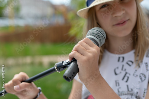 Young girl holding mic with two hands. Microphone and unrecognizable girl singer close up. Cropped image of female teen singer in the park. Copyspace