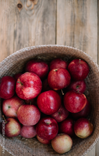 Delicious freshly harvested organic autumn red apples inside a wicker basket  stand-in on the wooden table  close up view