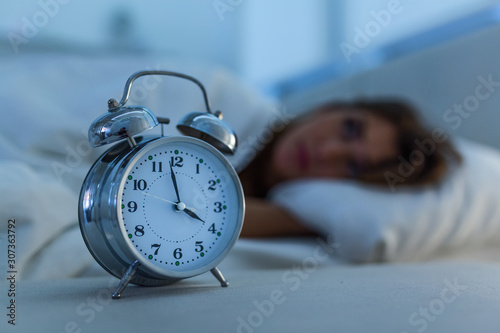 Sleepless and desperate beautiful caucasian woman awake at night not able to sleep, feeling frustrated and worried looking at clock suffering from insomnia in sleep disorder concept.